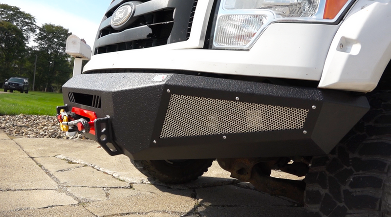 Load image into Gallery viewer, Alt text: &quot;Close-up view of a Fishbone Offroad 2009-2014 F-150 Pelican Front Bumper installed on a Ford truck, featuring rugged design with mesh grille and integrated winch mount.&quot;
