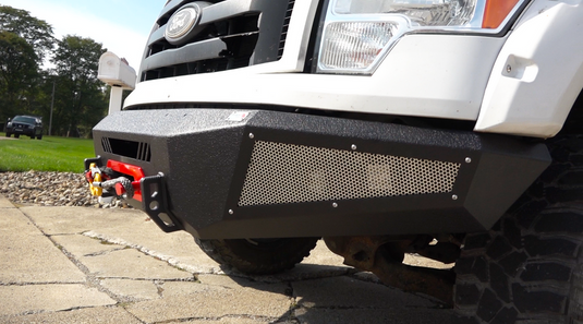 Alt text: "Close-up view of a Fishbone Offroad 2009-2014 F-150 Pelican Front Bumper installed on a Ford truck, featuring rugged design with mesh grille and integrated winch mount."