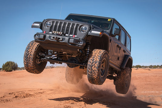 Jeep equipped with ICON Vehicle Dynamics Rebound satin black wheels performing an off-road jump in a desert setting