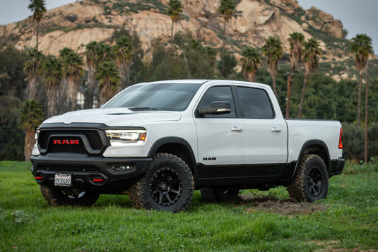 White RAM pickup truck equipped with ICON Vehicle Dynamics Rebound wheels in bronze, parked outdoors with hills in the background.