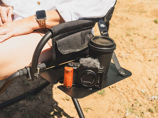 "Front Runner Expander Chair with attached Side Table holding a camera, travel mug, and personal accessories outdoors"