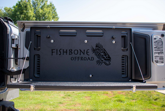 Alt text: "Fishbone Offroad tailgate table installed on a Jeep, compatible with JK, JKU, JL, JLU Wrangler and Ford Bronco models."