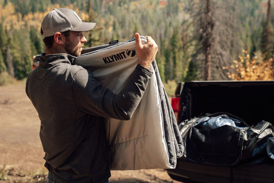 Man examining Klymit Horizon Overland Blanket near open trunk in nature setting