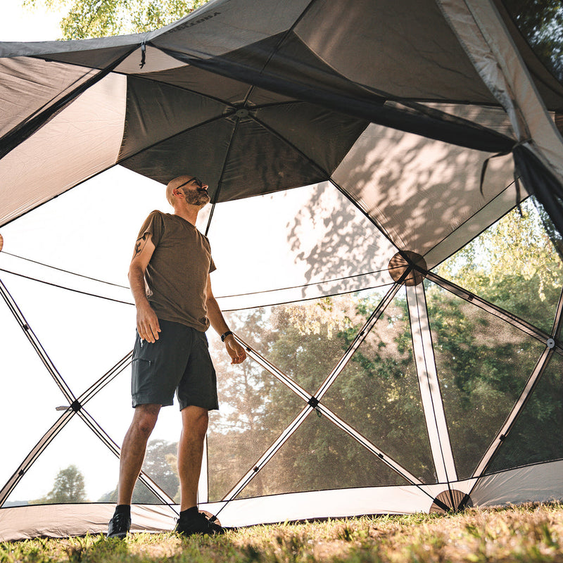 Load image into Gallery viewer, Man standing inside a Territory Tents 6-Sided Screen Tent set up in a sunny outdoor environment.
