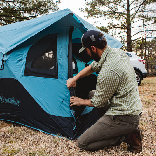Man setting up blue Gazelle T3X Overland Edition Tent outdoors near vehicle