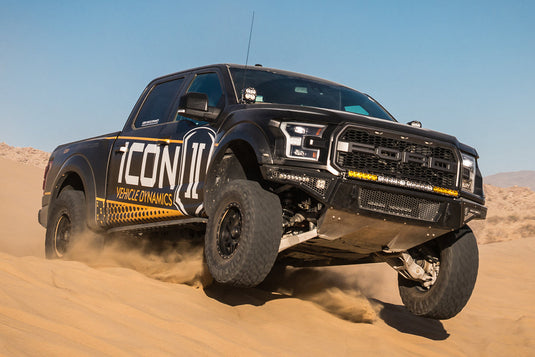 Black off-road pickup truck with ICON Vehicle Dynamics livery and gunmetal wheels with a black ring, showcasing suspension in desert terrain.