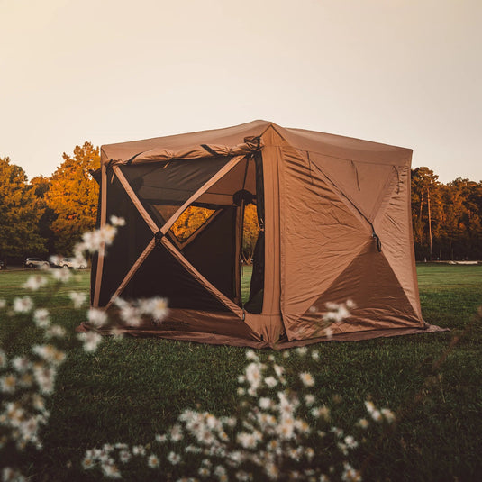 Gazelle Tents G6 Deluxe 6-Sided Portable Gazebo set up in a field at dusk with trees in the background, highlighting spacious design and easy access.