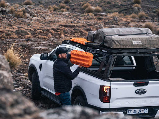 "Man using Front Runner Pro Bed Universal Accessory Mount on a white pickup truck in an outdoor setting"