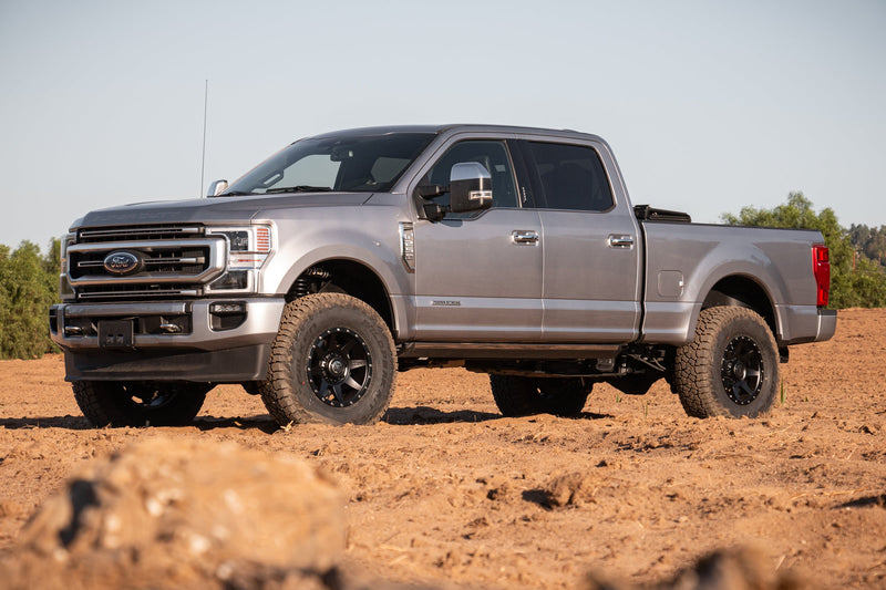 Load image into Gallery viewer, Silver Ford truck equipped with ICON Vehicle Dynamics Rebound HD wheels in Satin Black finish parked on rugged terrain.
