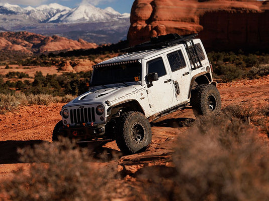 "White Jeep Wrangler JK equipped with Front Runner side mount ladder, off-roading in a mountainous desert landscape"