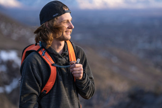 Man smiling while wearing Klymit Echo 12L Hydration Pack outdoors with scenic mountain view in background