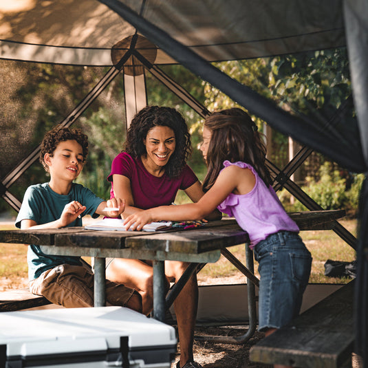 "Family enjoying a picnic under a Territory Tents 6-Sided Screen Tent at a campsite"