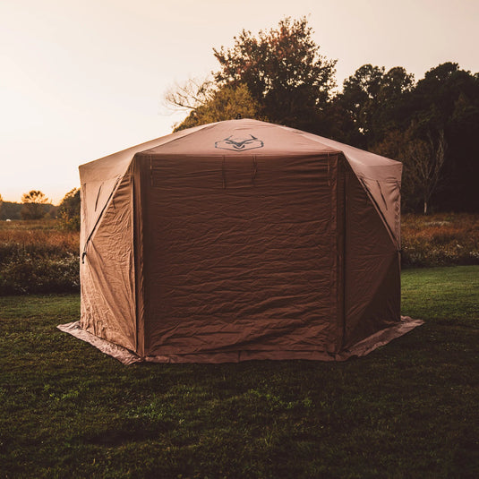 Gazelle Tents G6 Deluxe 6-Sided Portable Gazebo set up on grass with trees in the background during dusk.