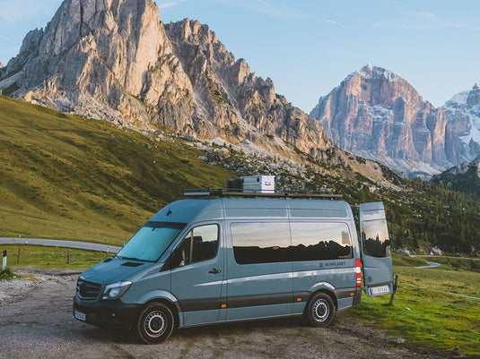 Mercedes Benz Sprinter with Front Runner Slimline II Roof Rack Kit parked in a mountainous region at sunset.