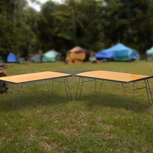 inchOverland Vehicle Systems portable camping tables with wood base set up outdoors near tents at a campsiteinch