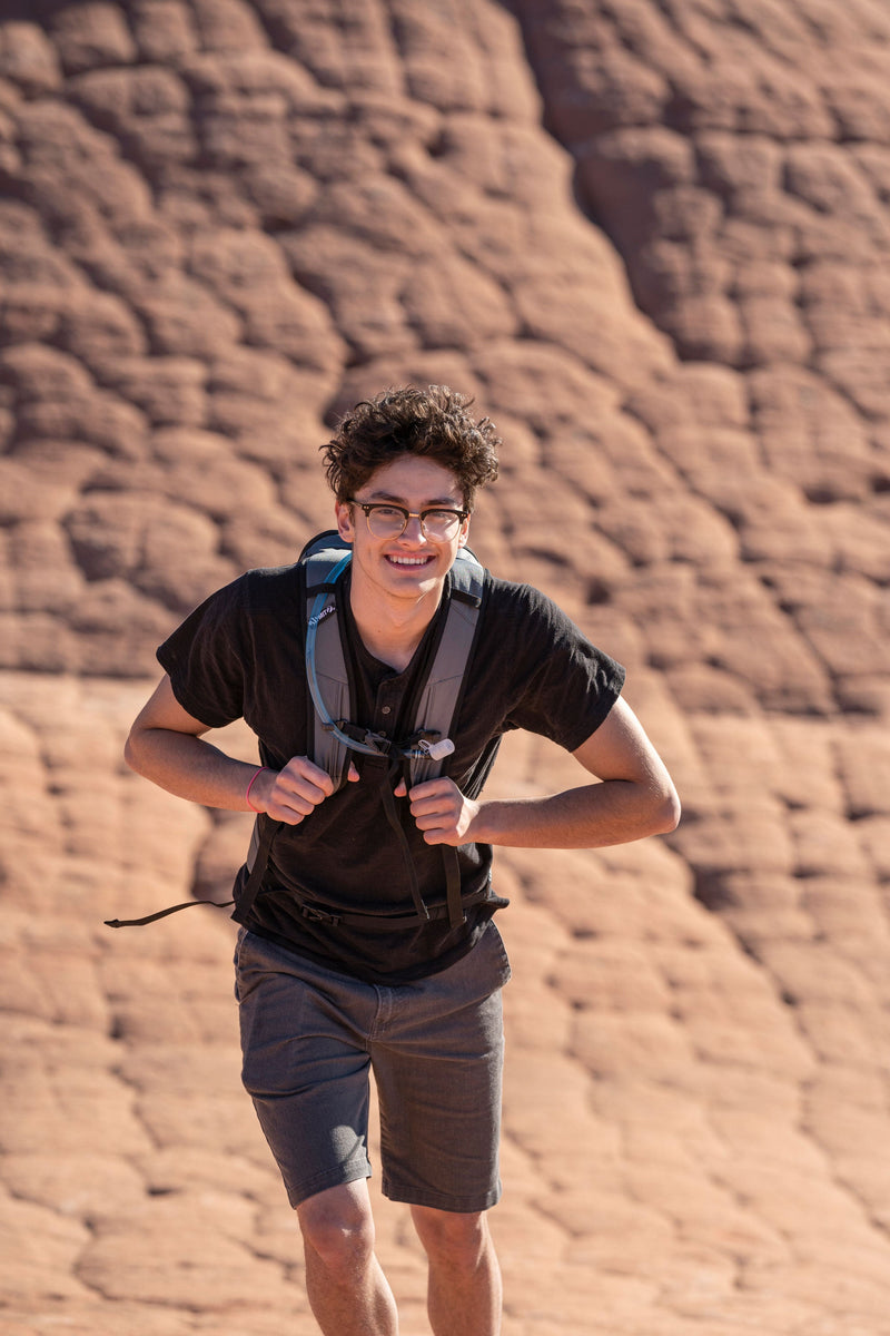 Load image into Gallery viewer, Smiling hiker wearing Klymit Echo 12L Hydration Pack on a desert trail
