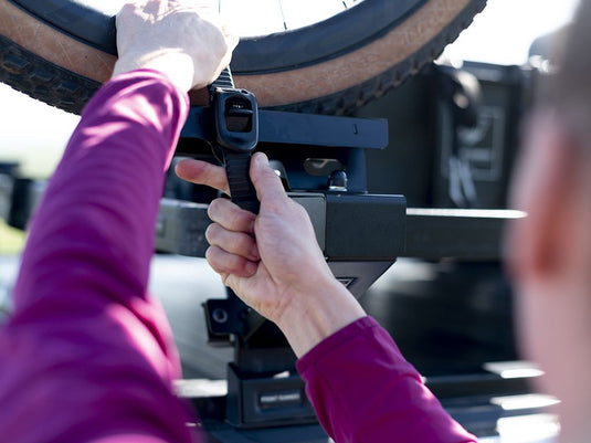 Person attaching a bike tire to the Front Runner Load Bed Rack Side Mount designed for secure bicycle transport